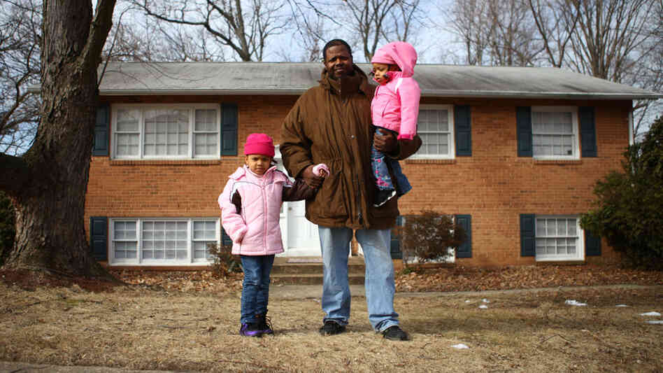 Robert  Adams carries his daughter Layla, 2, and walks with Lucy, 4, in front of their home in District Heights, Md. Adams grew up near the Anacostia Historic District  of Washington, D.C., but couldn't afford to buy a home  there for his family. He now lives in this suburb, a few miles away from his mother and  grandmother, who still live in the house where he grew up.