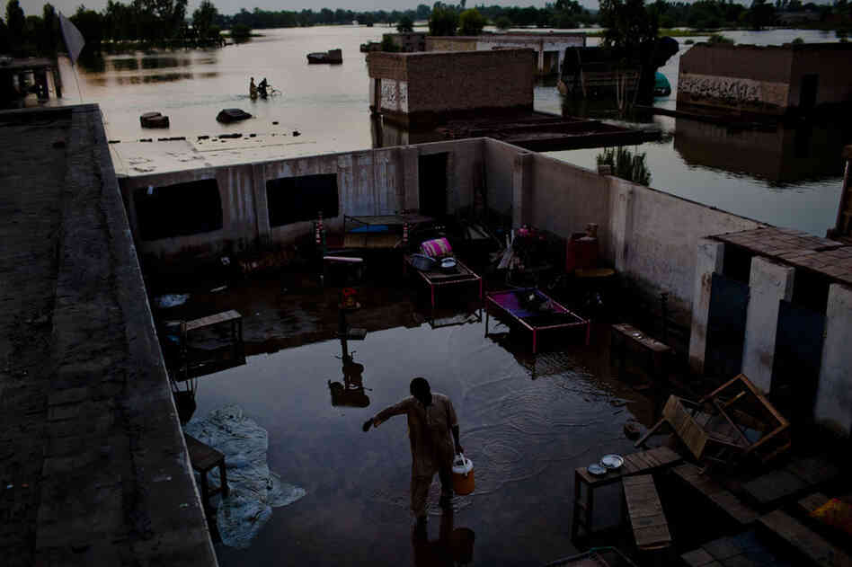 A boy walks through a flooded yard carrying water prior to Maghrib prayer and Iftar or breaking fast as it is called during the month of Ramadan on August 21, 2010 in the village of Vasandawali south of Muzaffargarh in Punjab, Pakistan.