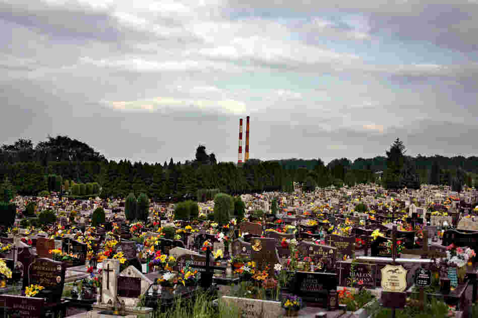 A modern cemetery in the town of Oswiecim, with smokestacks from the town's chemical factory looming in the distance. The factory was built by Nazi Germany during the war and used prisoners from Auschwitz to run it.