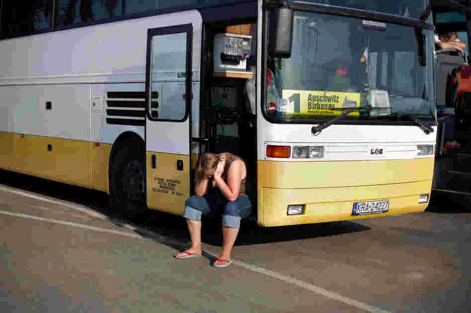 A tourist at Auschwitz II-Birkenau sits at a tour bus in the parking lot by the entrance.