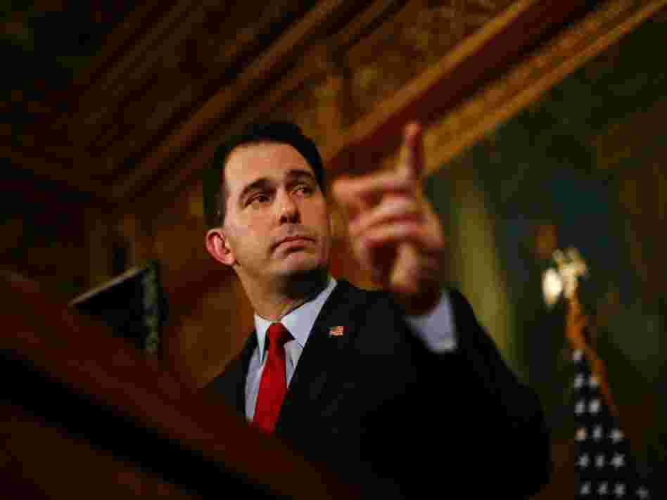 Republican Gov. Scott Walker speaks at a  news conference inside the Wisconsin State Capitol in Madison on Feb. 21 while people protest the legislation proposed by Walker to restrict collective bargaining.