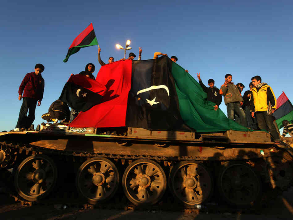 Anti-Gadhafi protesters wave their old national flag as they stand atop an abandoned army tank in the eastern Libyan city of Benghazi on Monday.