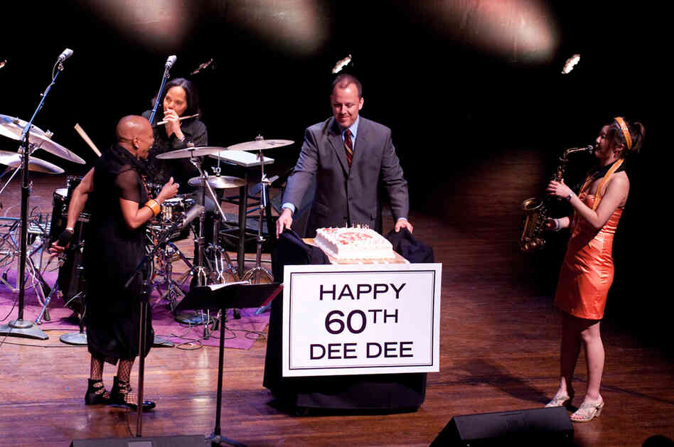 Kevin Struthers, director of jazz programming at the Kennedy Center, presents a birthday cake to Dee Dee Bridgewater, with Terri Lyne Carrington (drums) and Grace Kelly (saxophone) looking on.