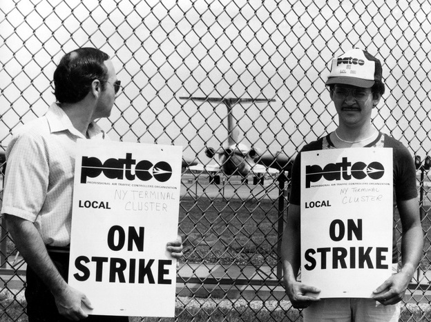 Striking air traffic controllers stand on a picket line as an airliner taxis on the runway behind them at New York's La Guardia Airport, Aug. 6, 1981.