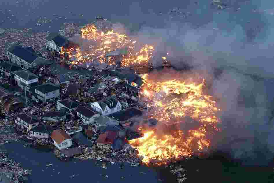 Houses burn while the Natori river floods in Natori City, Miyagi prefecture. 