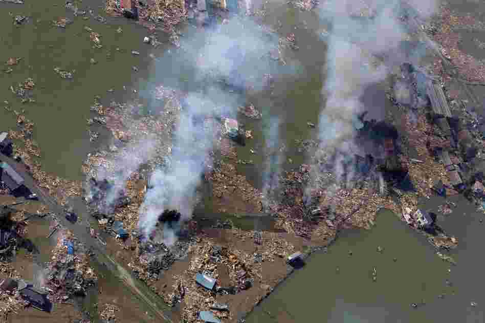 Smoke rises over a flooded area in Sendai. 