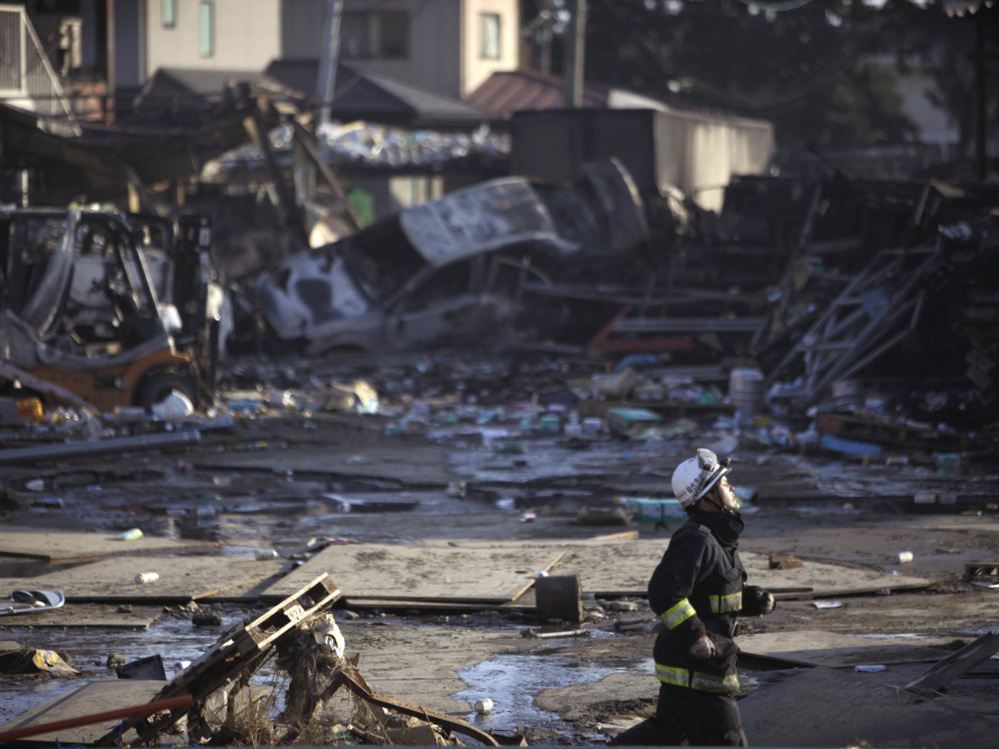 A firefighter runs against a background of damage from  a massive tsunami triggered by a powerful earthquake in Sendai in northern Japan.