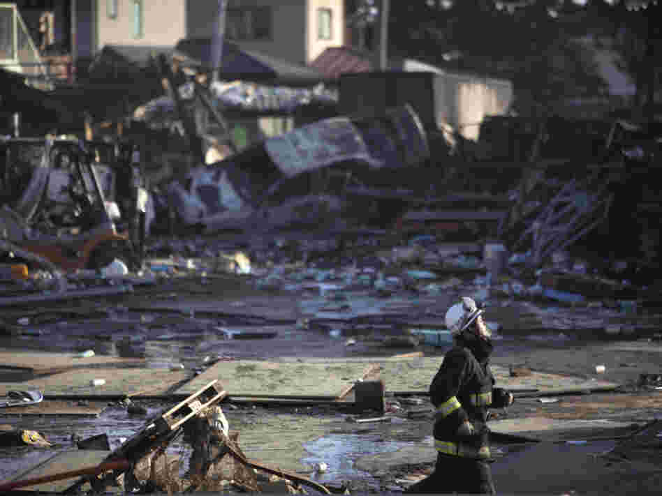 A firefighter runs against a background of damage from  a massive tsunami triggered by a powerful earthquake in Sendai in northern Japan.