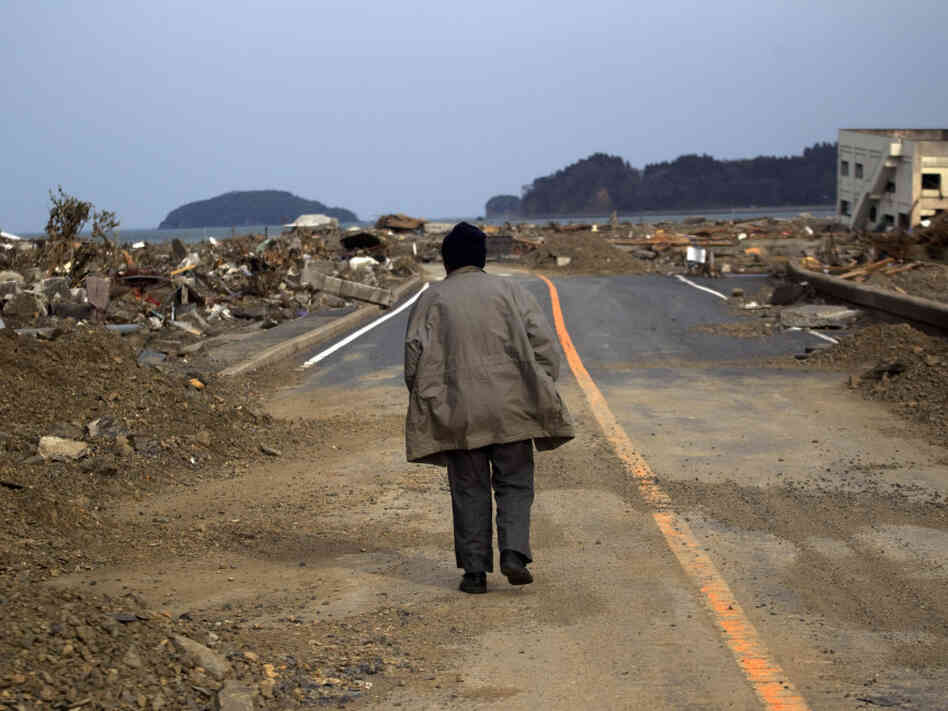 A Japanese earthquake and tsunami survivor walks alone Monday on a road past the destroyed village of Saito in northeastern Japan.