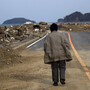 A Japanese earthquake and tsunami survivor walks alone Monday on a road past the destroyed village of Saito in northeastern Japan.