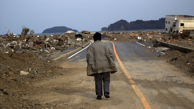 A Japanese earthquake and tsunami survivor walks alone Monday on a road past the destroyed village of Saito in northeastern Japan.