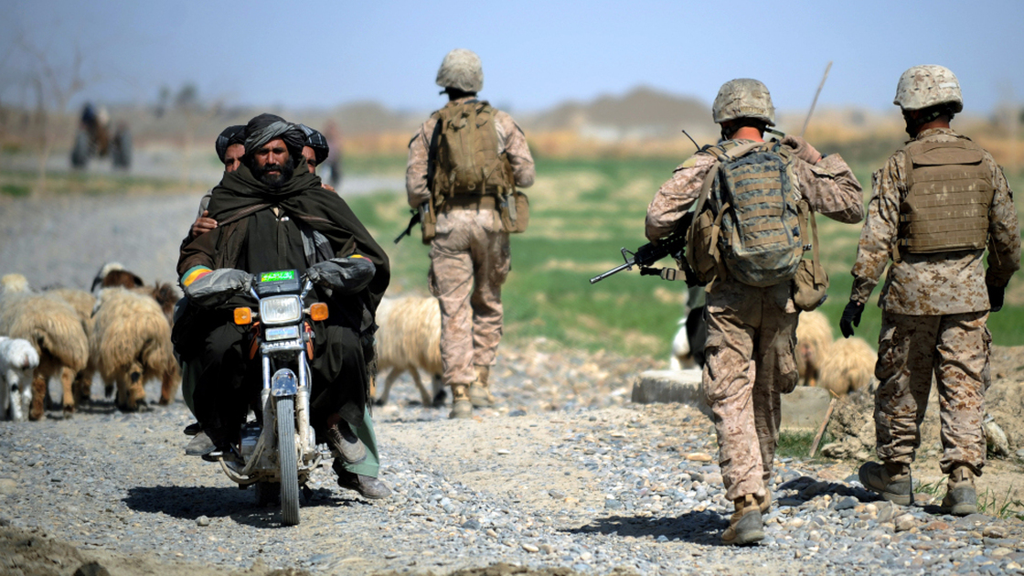 Three Afghan men on a motorcycle passed by as U.S. Marines patrolled last month in Afghanistan's Helmand Province.