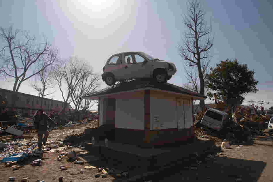A car, washed into the area by the tsunami, sits on top of a small building in a destroyed neighborhood in Sendai, Japan. 