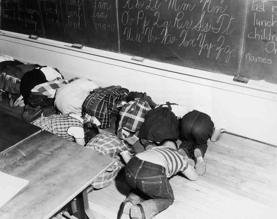 Schoolchildren kneel to practice a "duck and cover" air-raid drill in an elementary school classroom, circa 1955. Schoolchildren kneel to practice a "duck and cover" air-raid drill in an elementary school classroom, circa 1955.
