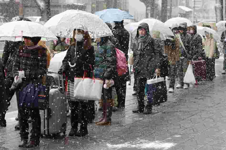 People wait in the snow for a bus to leave town in Sendai, Japan. 