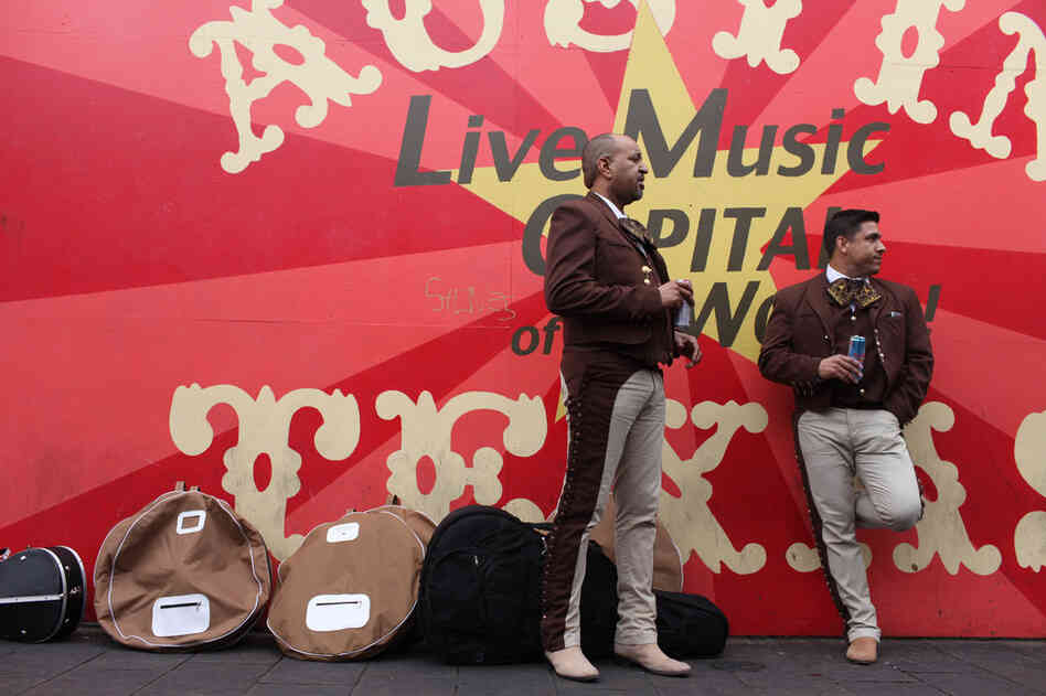 Mariachi musicians taking a breather against an iconic mural celebrating Austin's live music scene. 