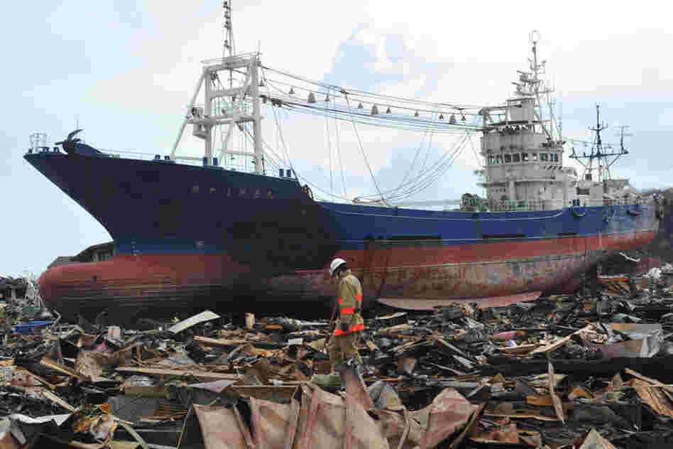 Japanese rescuers search through debris in front of a large ship washed ashore in Kesennuma, Miyagi prefecture. 