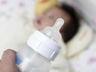 A baby bottle with an infant seen in the background. A baby bottle with an infant seen in the background.