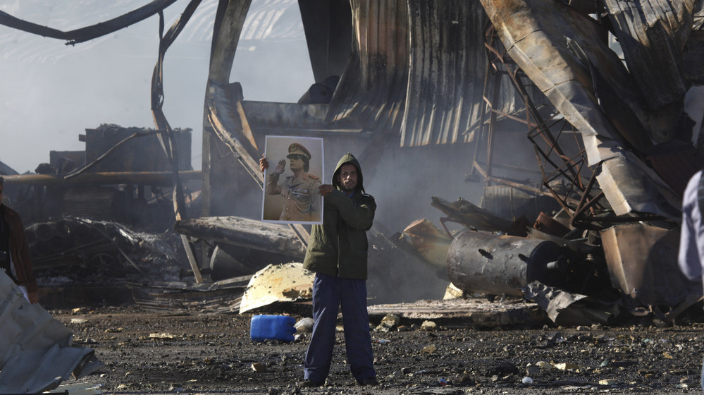 A Libyan supporter of Moammar Gadhafi stands amid the wreckage of what was described as a maintenance warehouse  at a naval base in Tripoli that was hit by coalition missiles.