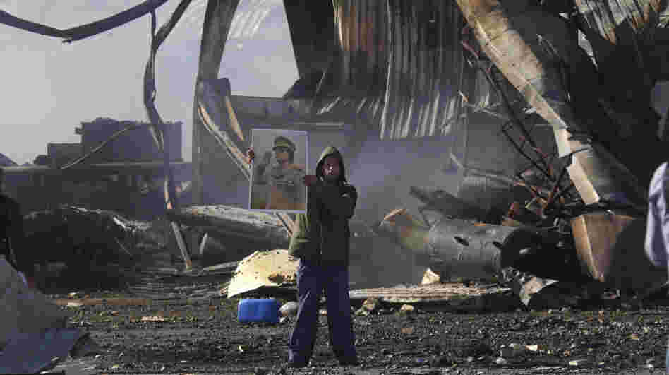 A Libyan supporter of Moammar Gadhafi stands amid the wreckage of what was described as a maintenance warehouse  at a naval base in Tripoli that was hit by coalition missiles.