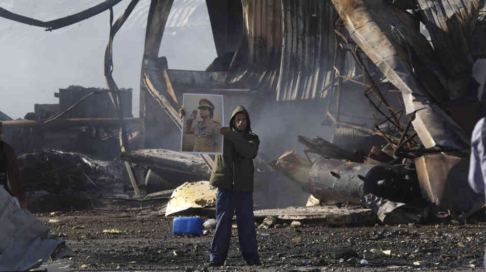 A Libyan supporter of Moammar Gadhafi stands amid the wreckage of what was described as a maintenance warehouse  at a naval base in Tripoli that was hit by coalition missiles.