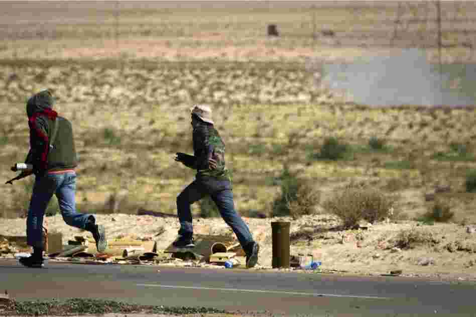 Rebels run to take cover as a mortar, seen at top right, from Gadhafi's forces is fired on them on the outskirts of Ajdabiya. 