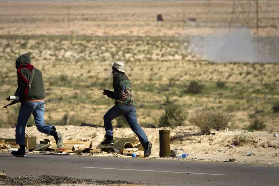 Rebels run to take cover as a mortar, seen at top right, from Gadhafi's forces is fired on them on the outskirts of Ajdabiya. 