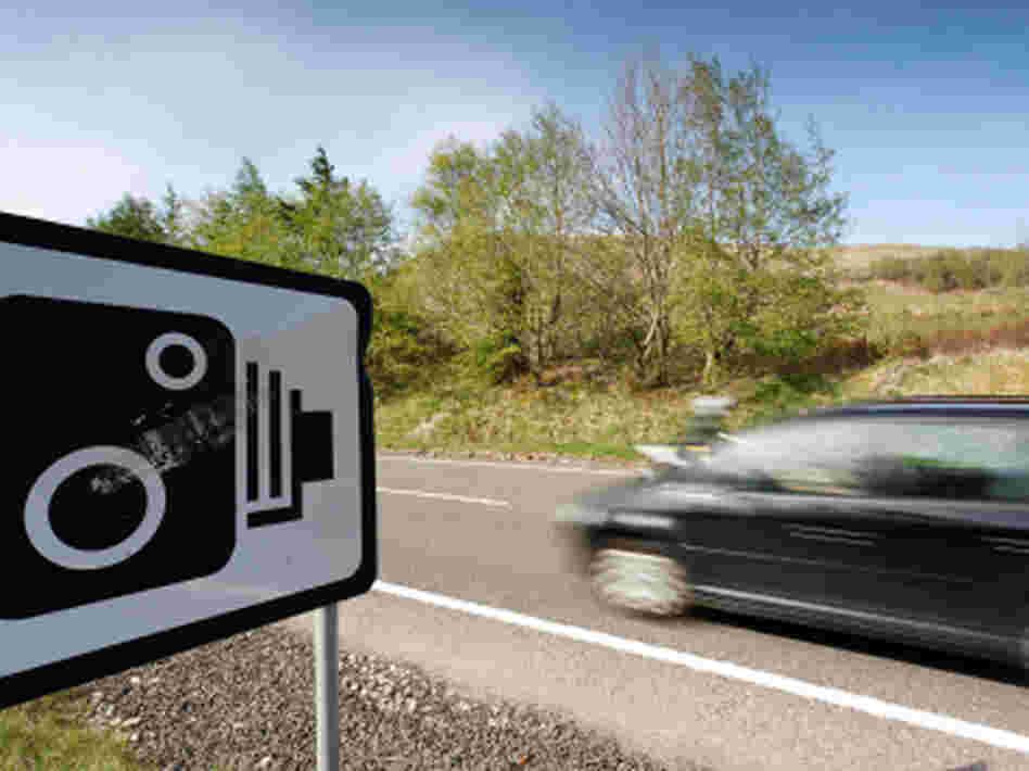 A car passes a warning sign for speed cameras. A car passes a warning sign for speed cameras.