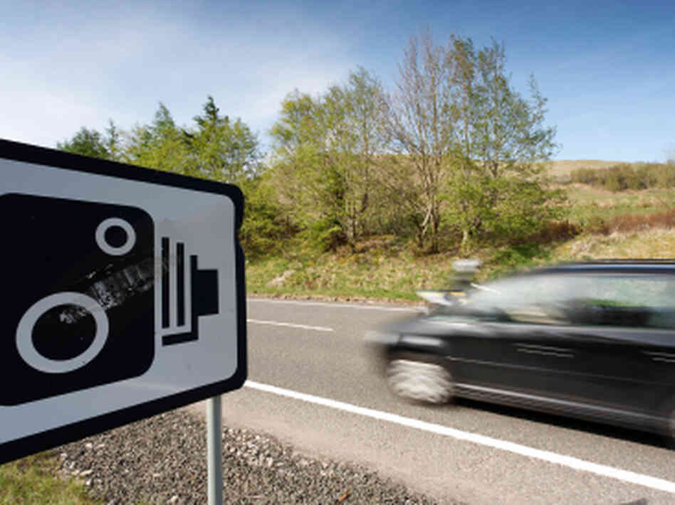 A car passes a warning sign for speed cameras. A car passes a warning sign for speed cameras.