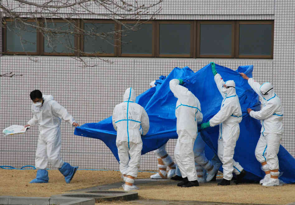 Japan Self-Defence Force officers in radiation protection suits hold a blue sheet over workers who were exposed this week to high levels of radiation at the Fukushima Dai-ichi plant.