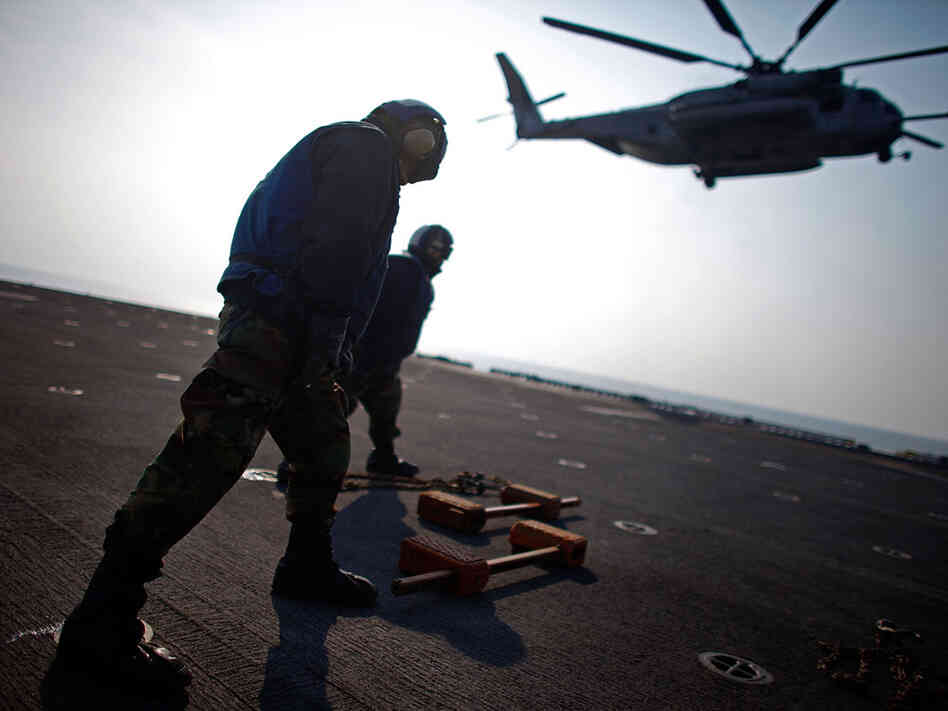 Crew members aboard the USS Essex brace against the rotor wash from a Marine helicopter that is also taking part in Operation Tomodachi. Crew members aboard the USS Essex brace against the rotor wash from a Marine helicopter that is also taking part in Operation Tomodachi.