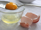 A yolk rests in a slotted spoon over a bowl containing the separated egg white, with the egg shell cracked alongside A yolk rests in a slotted spoon over a bowl containing the separated egg white, with the egg shell cracked alongside