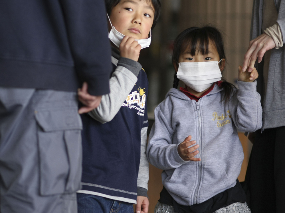 Children watch as their father is screened for radiation at a shelter in Fukushima prefecture, Japan. Plutonium is seeping from a damaged nuclear power plant into the soil outside, officials said Tuesday.