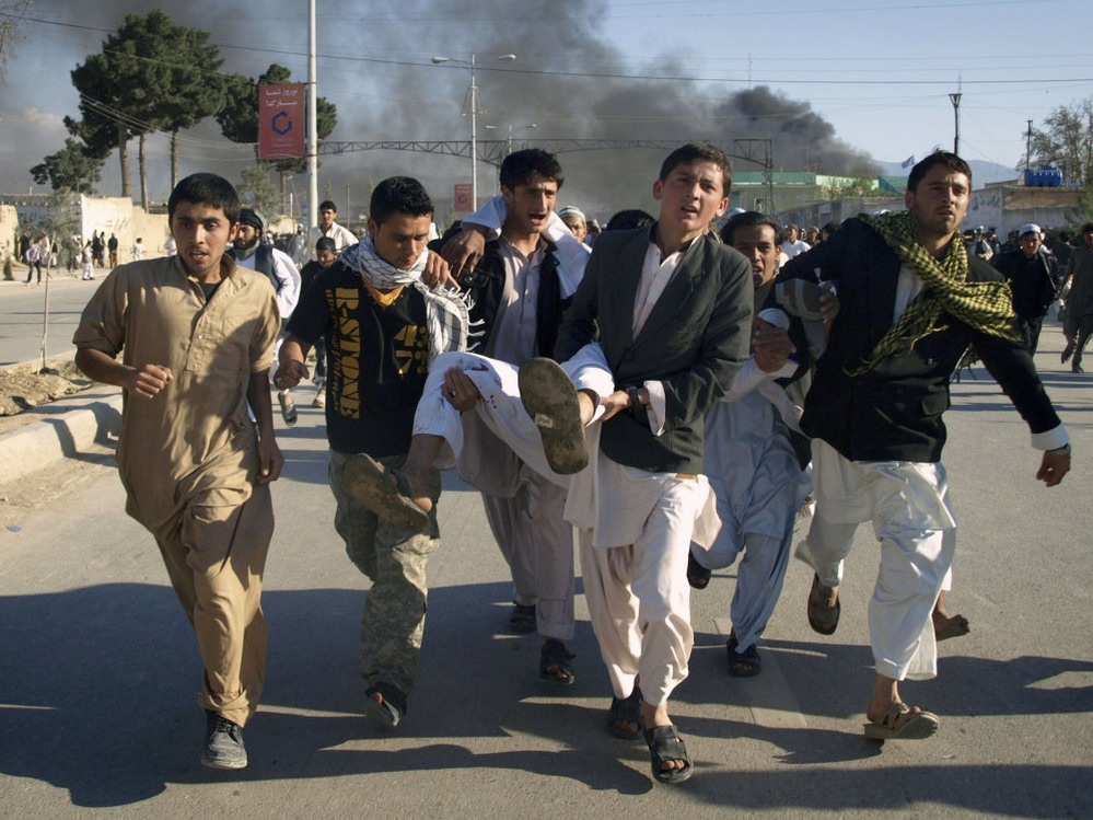 Afghans carrying a man who was wounded in an attack on the U.N.'s Mazar-i-Sharif office during a demonstration to condemn the burning of the Quran by a Florida pastor.