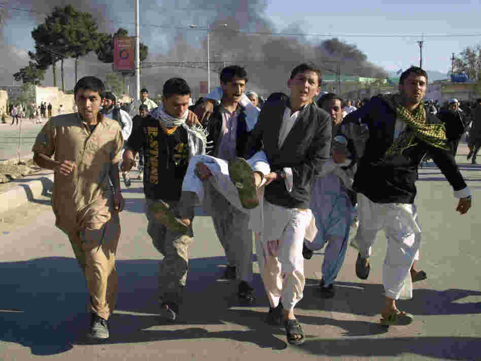 Afghans carrying a man who was wounded in an attack on the U.N.'s Mazar-i-Sharif office during a demonstration to condemn the burning of the Quran by a Florida pastor.