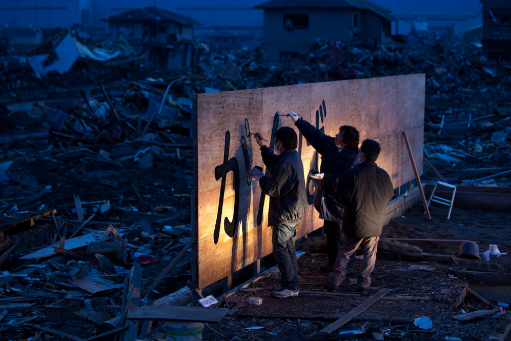 Tsunami survivor Kenichi Kurosawa (center) and his friends draw words that translate to "hang in there" on a billboard in Ishinomaki, Miyagi prefecture. 