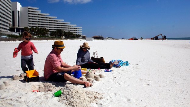 A family from New Orleans visits a beach in Pensacola, Fla., just before spring break season last month. In the distance, workers continue to clean up after the Deepwater Horizon oil spill.