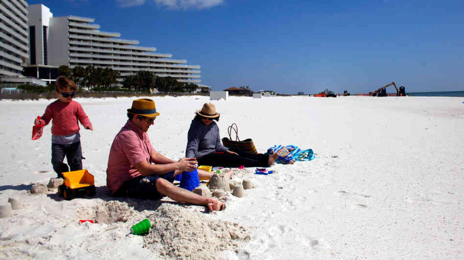 A family from New Orleans visits a beach in Pensacola, Fla., just before spring break season last month. In the distance, workers continue to clean up after the Deepwater Horizon oil spill.