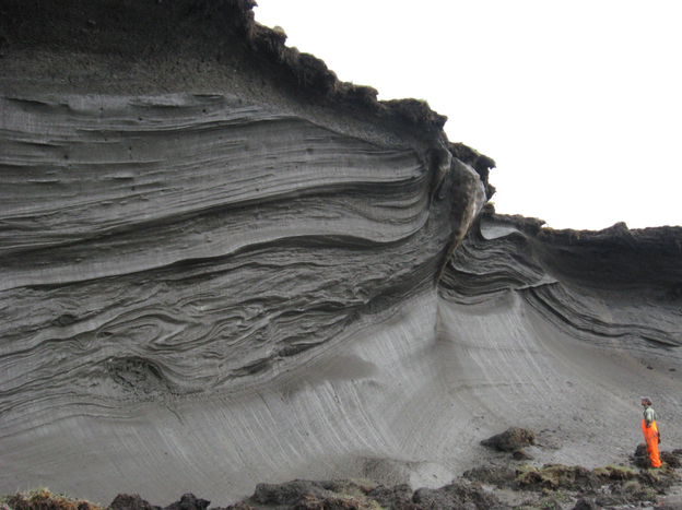 A scientist stands in front of an ice-rich permafrost exposure in the coastal zone of Herschel Island, Yukon Territory, Canada. Ice in the permafrost is melting, contributing to rapid erosion.