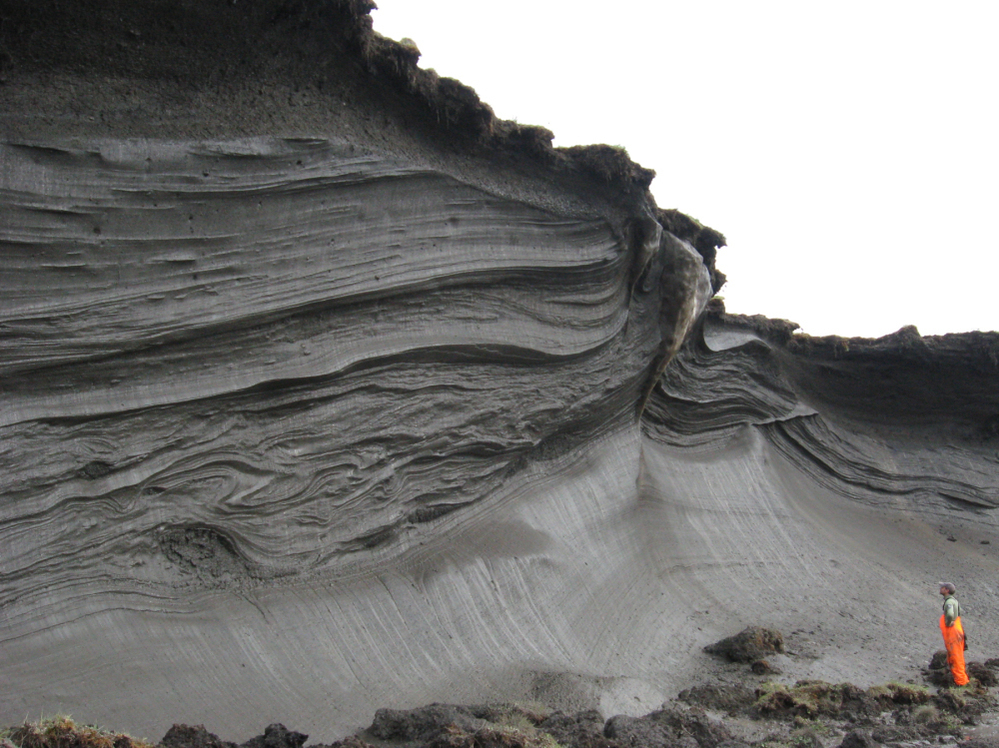 A scientist stands in front of an ice-rich permafrost exposure in the coastal zone of Herschel Island, Yukon Territory, Canada. Ice in the permafrost is melting, contributing to rapid erosion.