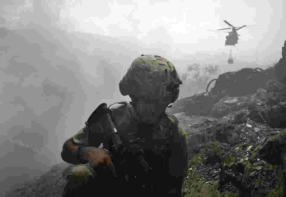 A soldier takes cover from the dust being generated by an incoming Chinook helicopter delivering supplies to the Restrepo base. The image is from Hetherington's book Infidel.