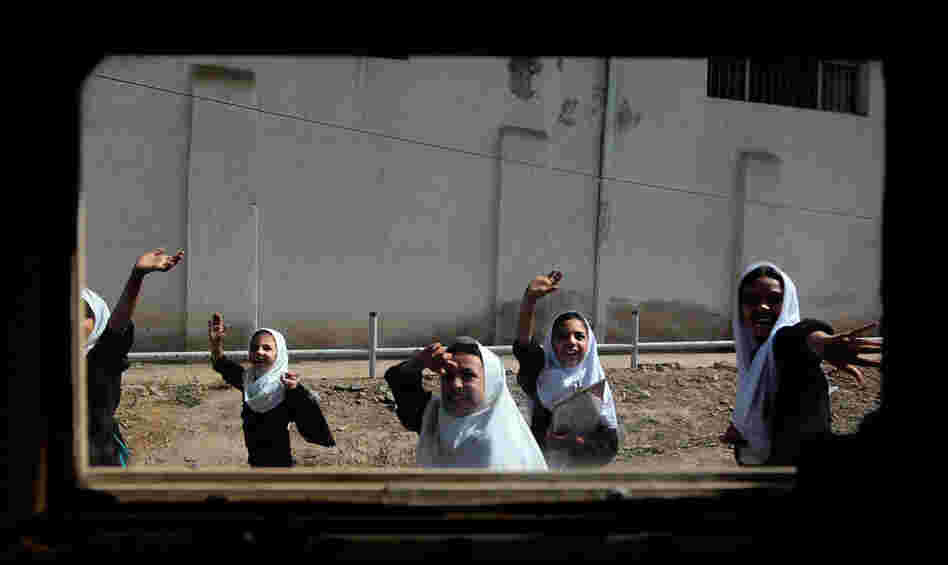 Afghan schoolgirls seen through the window of a Humvee wave to a passing American convoy in downtown Herat, Afghanistan, on June 26, 2010.