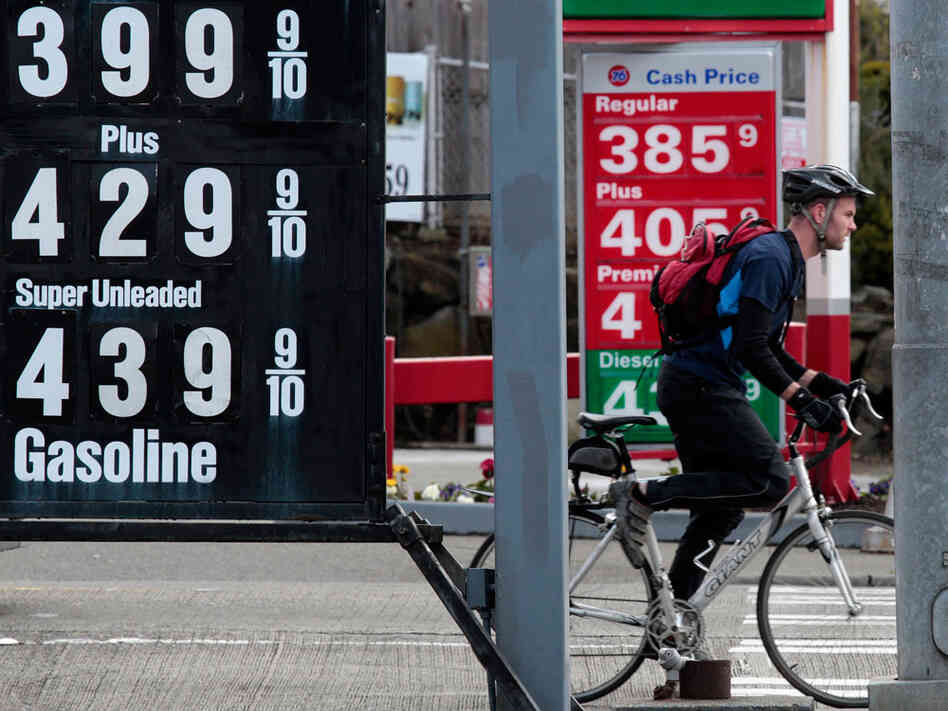 A bicyclist waits at an intersection between competing gas stations and multiple posted gas prices on Monday in Seattle. A bicyclist waits at an intersection between competing gas stations and multiple posted gas prices on Monday in Seattle.