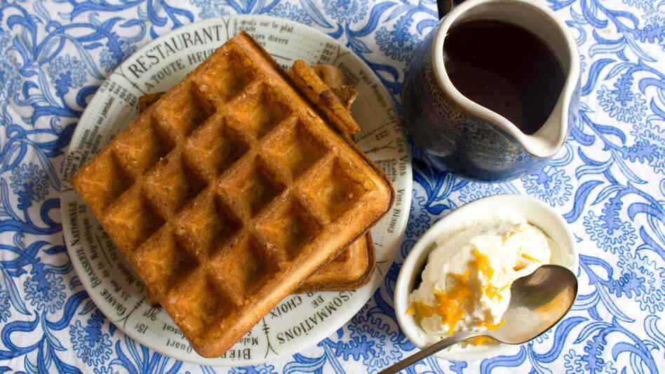 Belgian-style waffles on a plate, with a pitcher of maple syrup and a bowl of orange whipped cream on the side