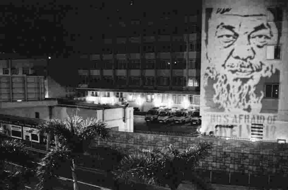 Flash graffiti of Ai Weiwei projected for a split second onto the Chinese People's Liberation Army barracks in Hong Kong. The PLA says this is a breach of the law.
