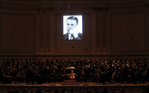 A short film displaying a picture of U.S. Secretary of Defense Robert McNamara is projected above members of the Dallas Symphony Orchestra during the performance.