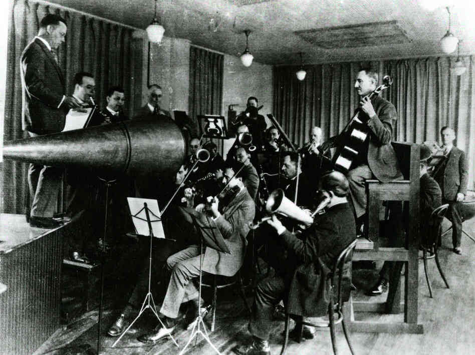The Victor Orchestra crowds around an enormous horn for an early acoustical recording session. The Victor Orchestra crowds around an enormous horn for an early acoustical recording session.