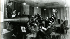 The Victor Orchestra crowds around an enormous horn for an early acoustical recording session. The Victor Orchestra crowds around an enormous horn for an early acoustical recording session.