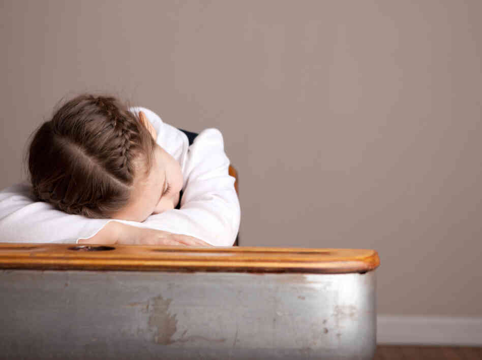 A sleepy girl snoozes at her school desk.