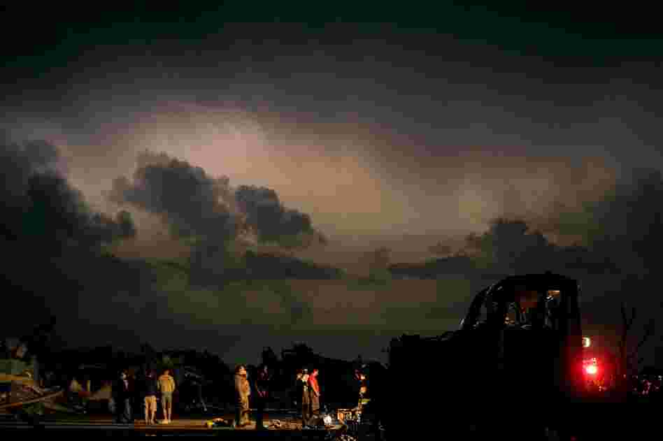 Emergency workers wait for a medical team after finding a body in a tornado-ravaged car. A twister tore through nearly six miles of the city Sunday. 
